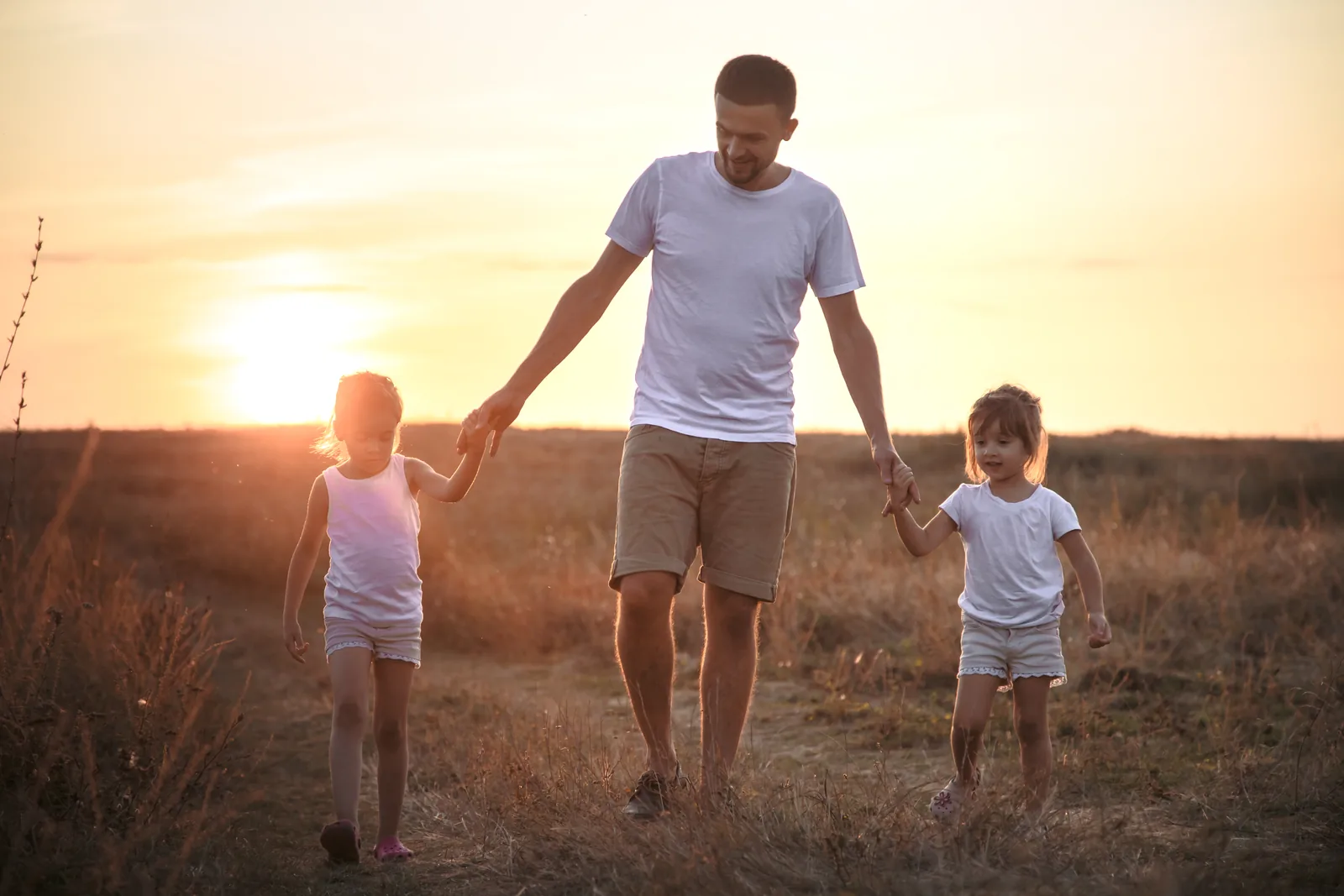 Un père et ses deux filles qui marchent au soleil couchant